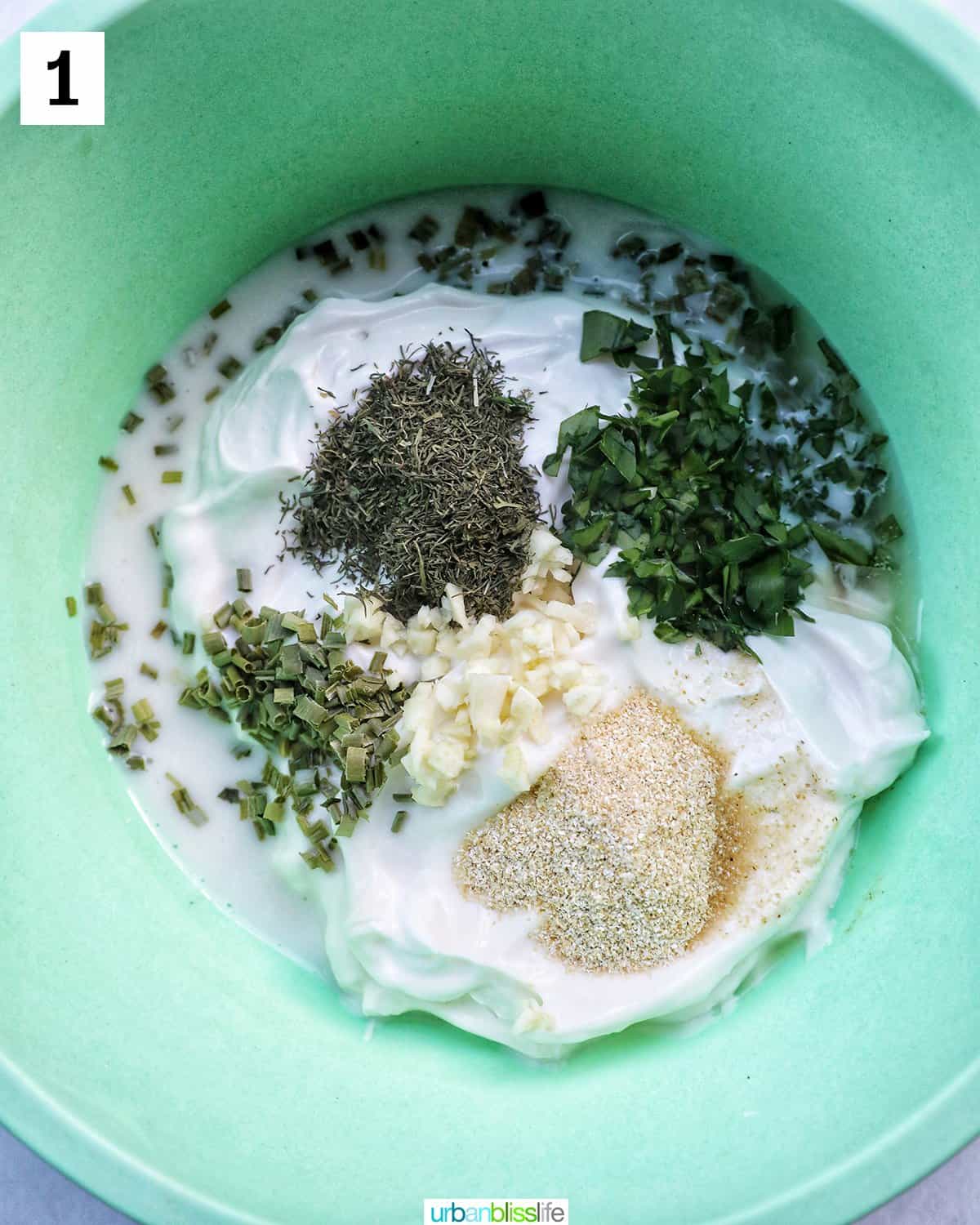 green bowl full of garlic, herbs, mayo, and sour cream to make ranch dressing.