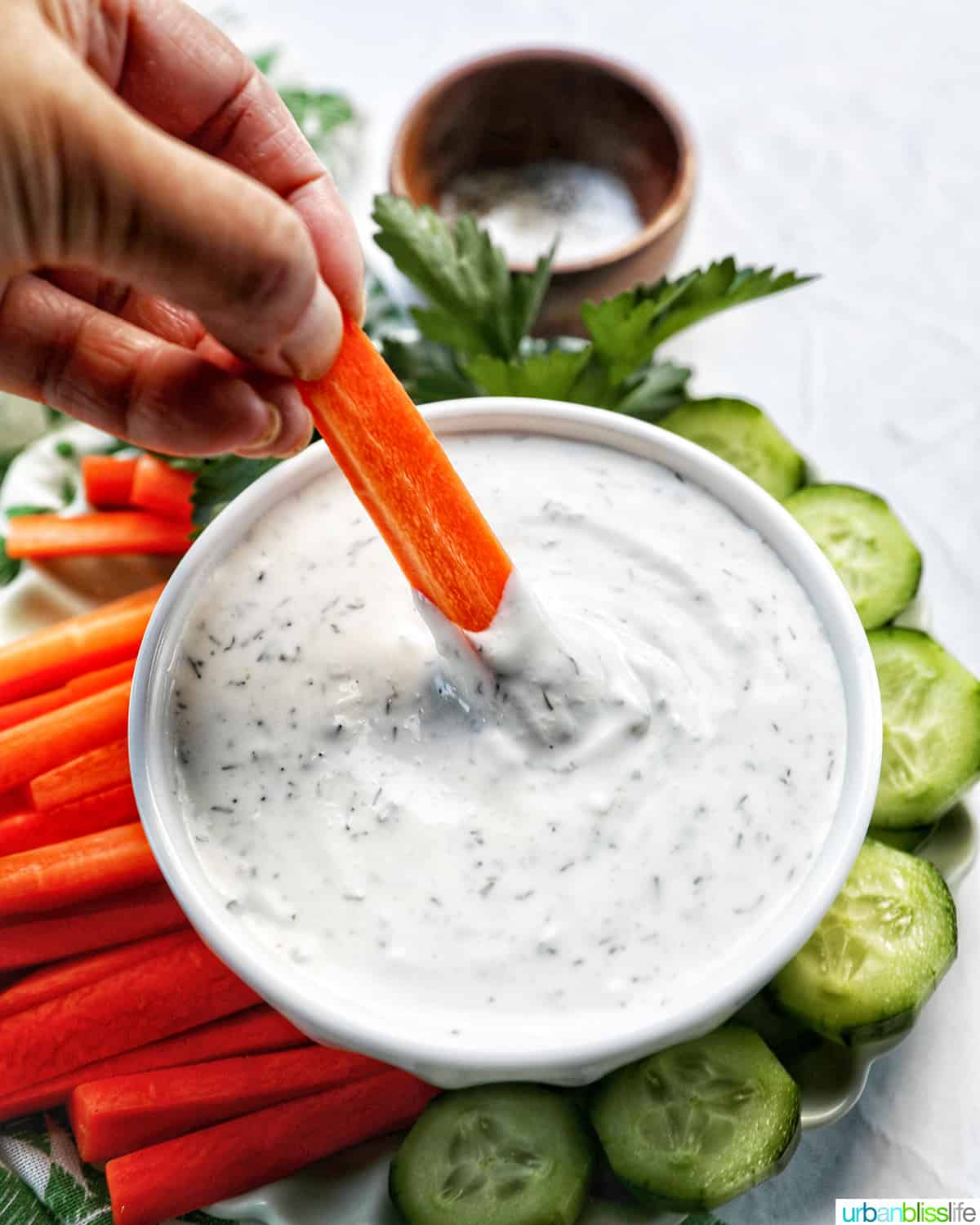 bowl of dairy free ranch dressing with carrot sticks, cucumber slices, and herbs.