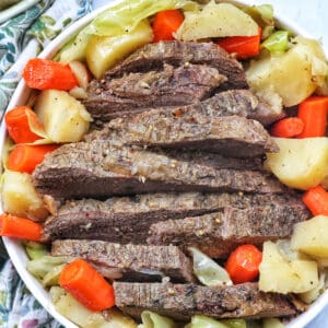bowl of sliced dutch oven brisket with carrots, potatoes, and cabbage.