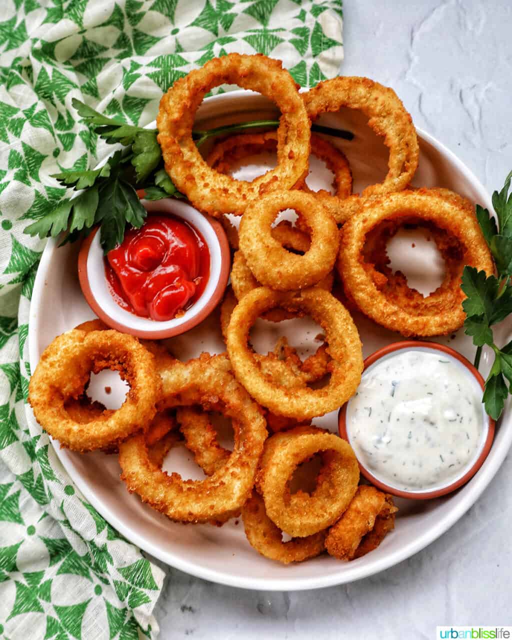 bowl of air fryer onion rings with sides of ranch dressing and ketchup..