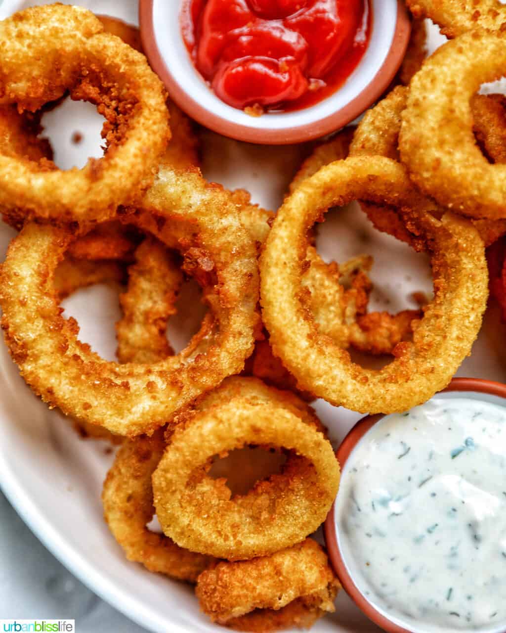 bowl of air fryer onion rings with sides of ranch dressing and ketchup..