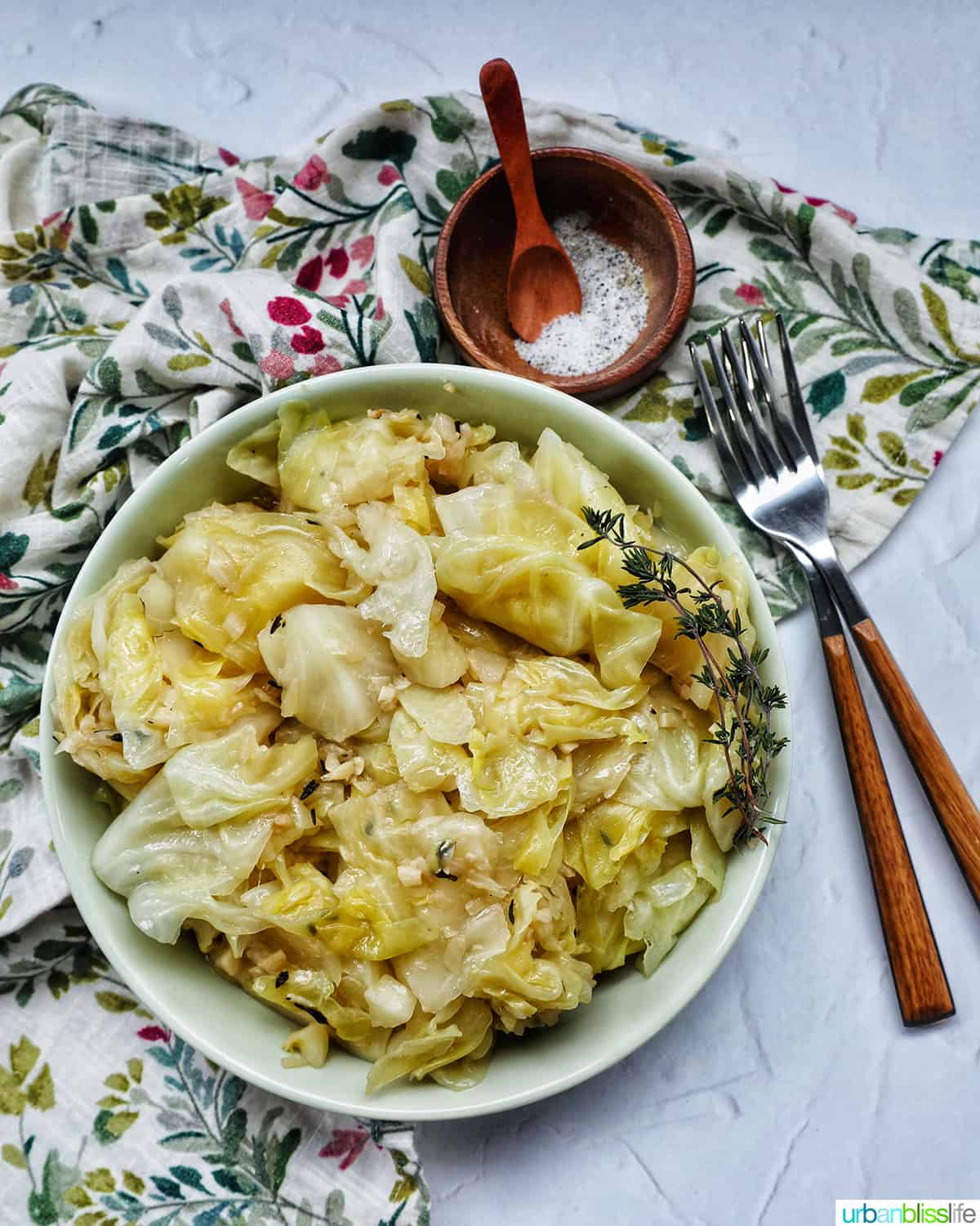 bowl of cooked instant pot cabbage with thyme sprigs, forks, and salt and pepper in a bowl.