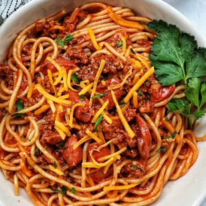 Jolibee spaghetti in a bowl with parsley, shredded cheese, and side of salt and pepper.