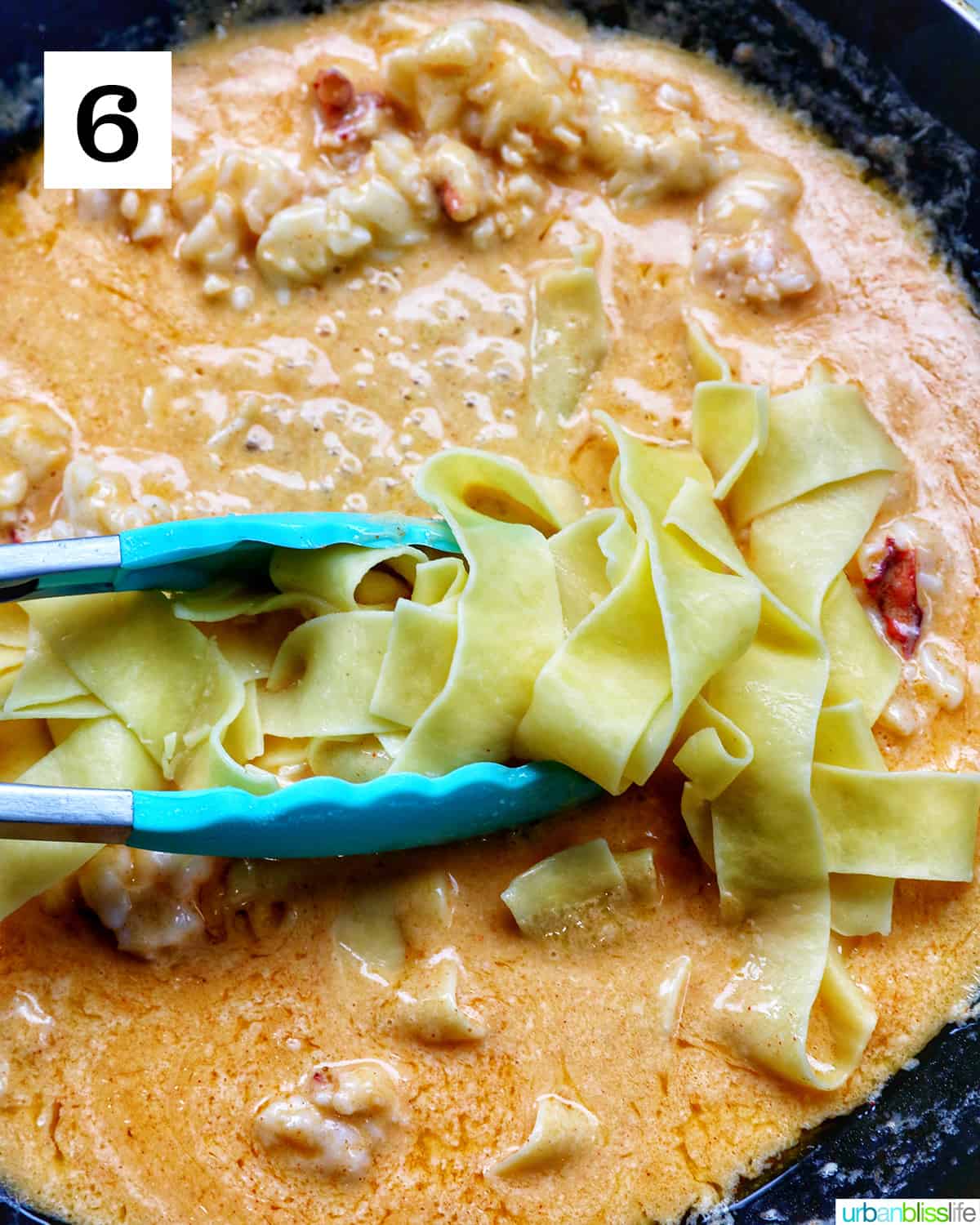 blue tongs adding pappardelle pasta to lobster sauce in a pan.