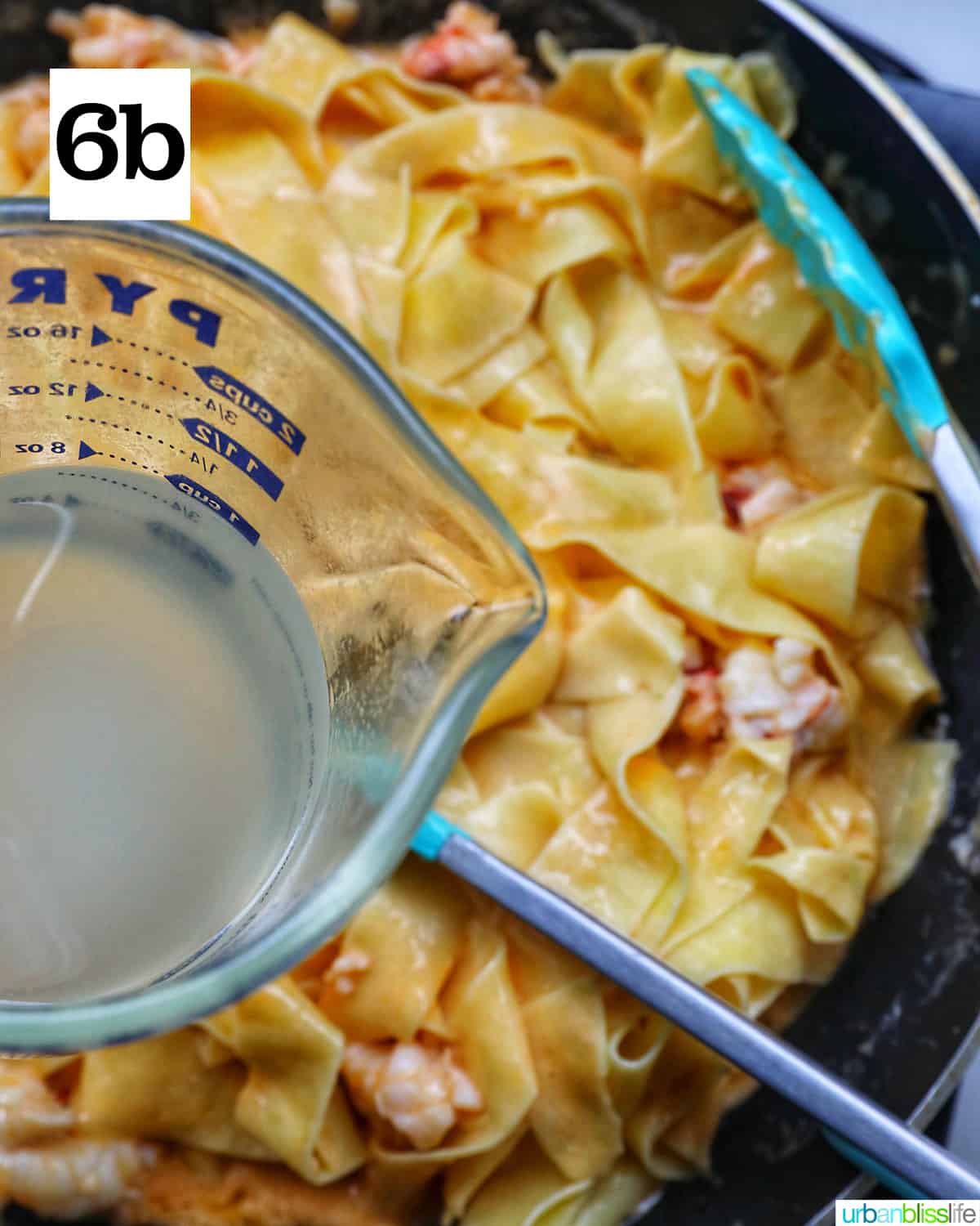 glass measuring cup with starchy pasta water over a pan of pappardelle pasta.