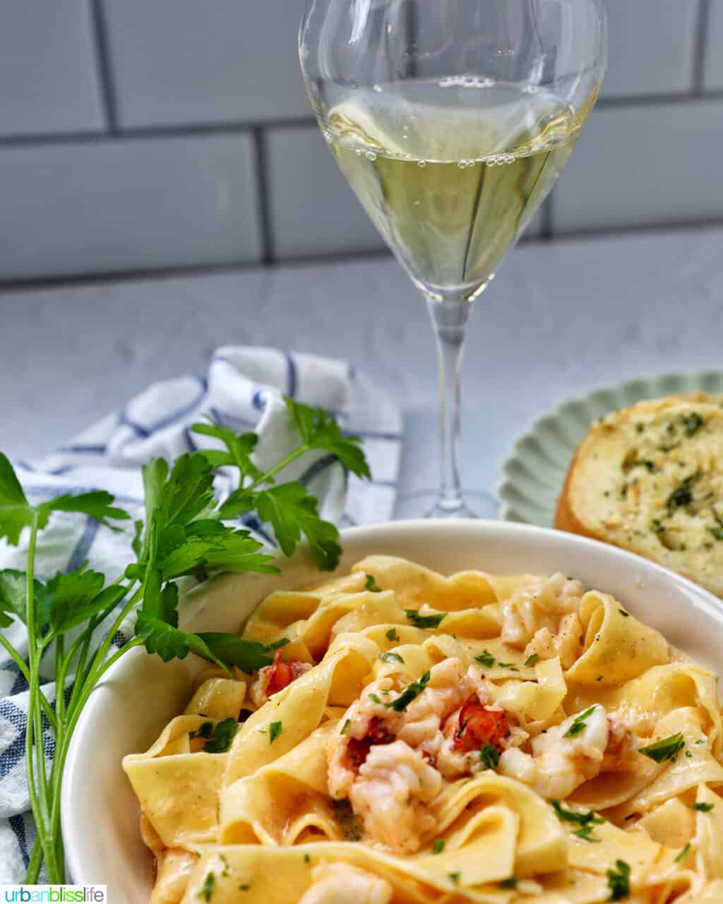 bowl of lobster pasta with side of parsley with glass of white wine.
