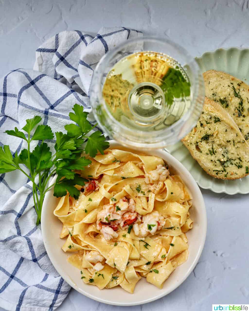bowl of lobster pasta with side of parsley with glass of white wine and side of garlic bread.