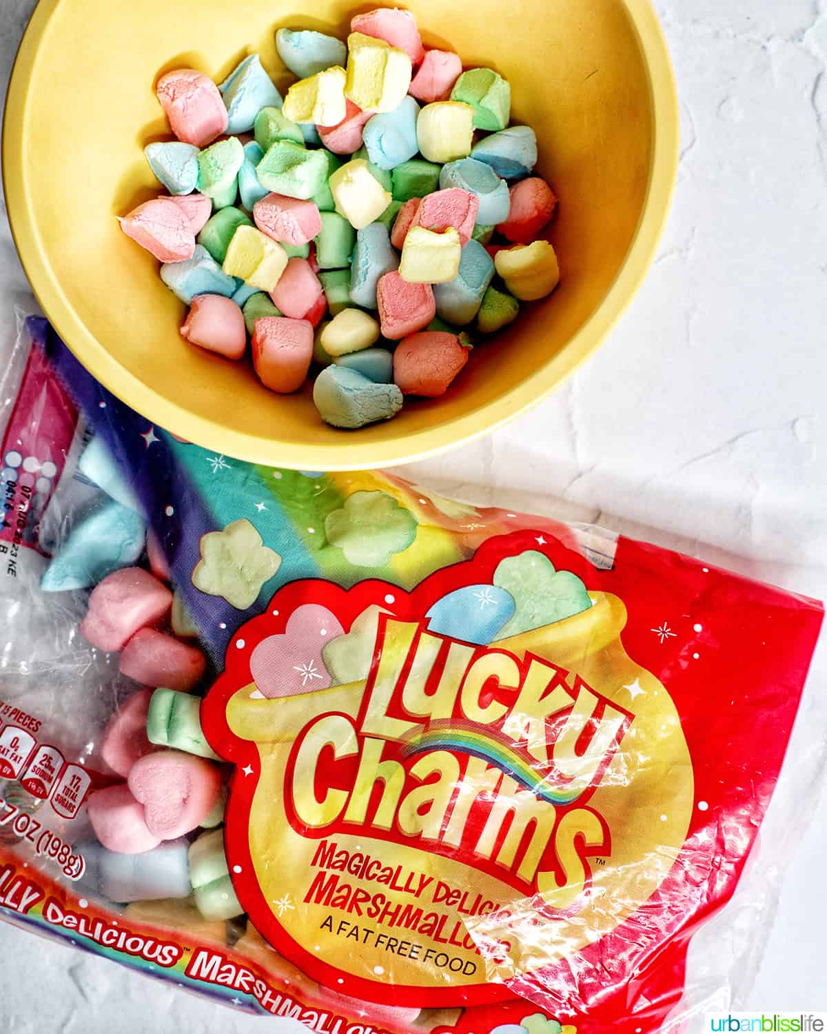 bowl of colorful Lucky Charms marshmallows next to a bag of Lucky Charms marshmallows.