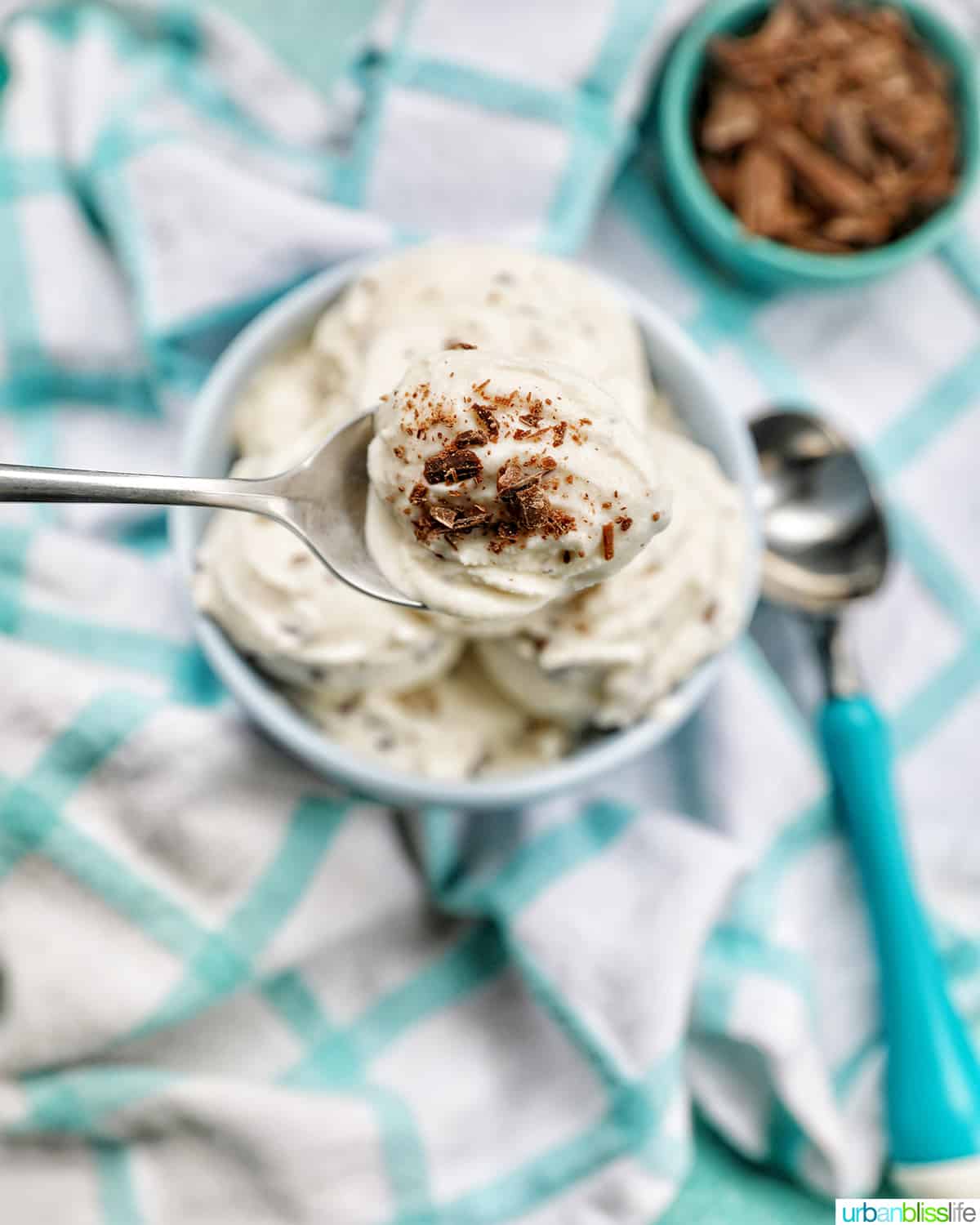 spoon scoop of bowl of stracciatella ice cream scoops with bowl of chocolate shavings on the side.