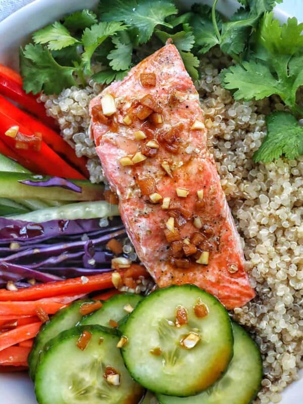 teriyaki salmon on a bed of quinoa with side of sliced colorful vegetables and a fork.