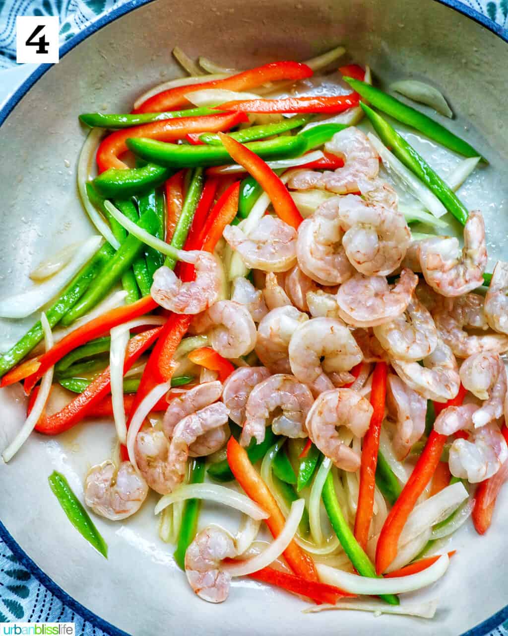adding shrimp to onions, red bell peppers, green bell peppers in a saucepan.