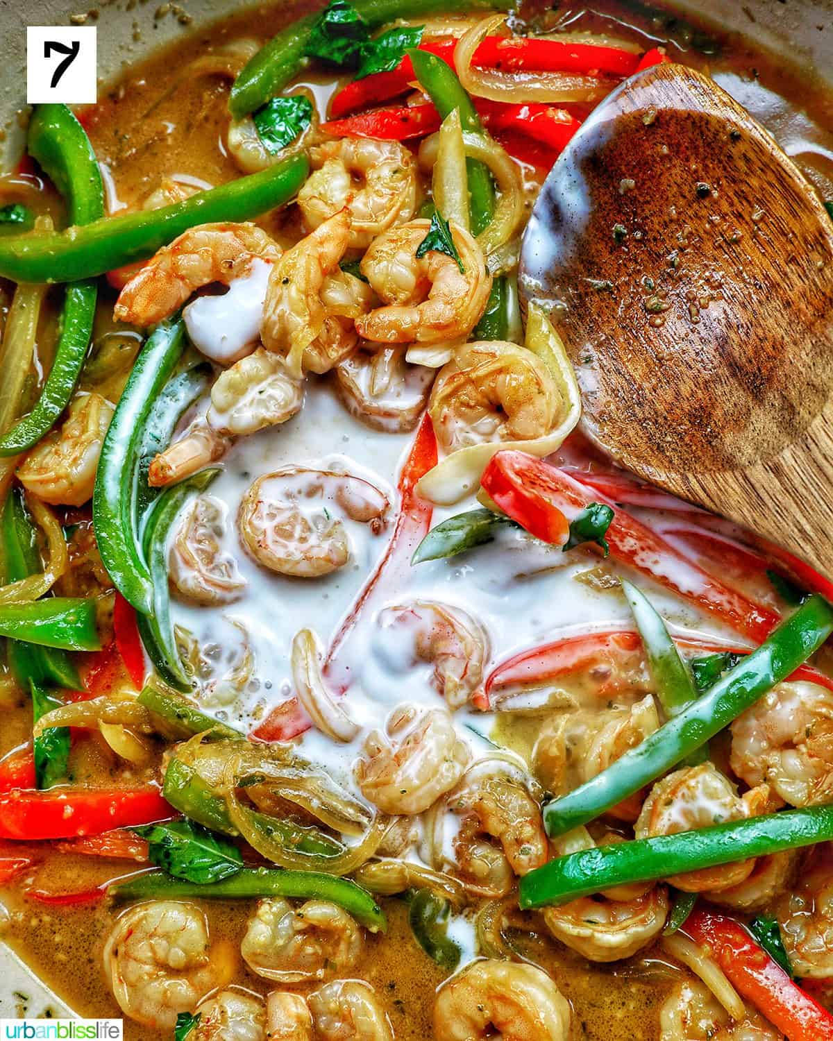 wooden spoon over sliced onions, red peppers, and green peppers in a saucepan.