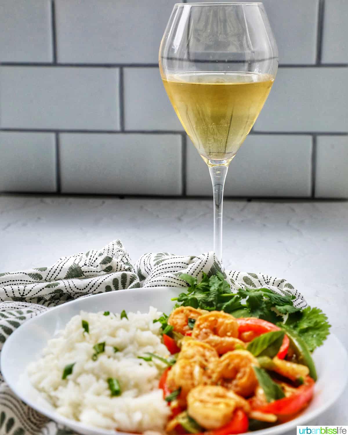 Thai Basil Shrimp with red and green peppers on a bed of rice with glass of white wine.