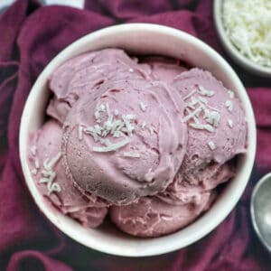 white bowl with scoops of purple ube ice cream topped with coconut flakes.