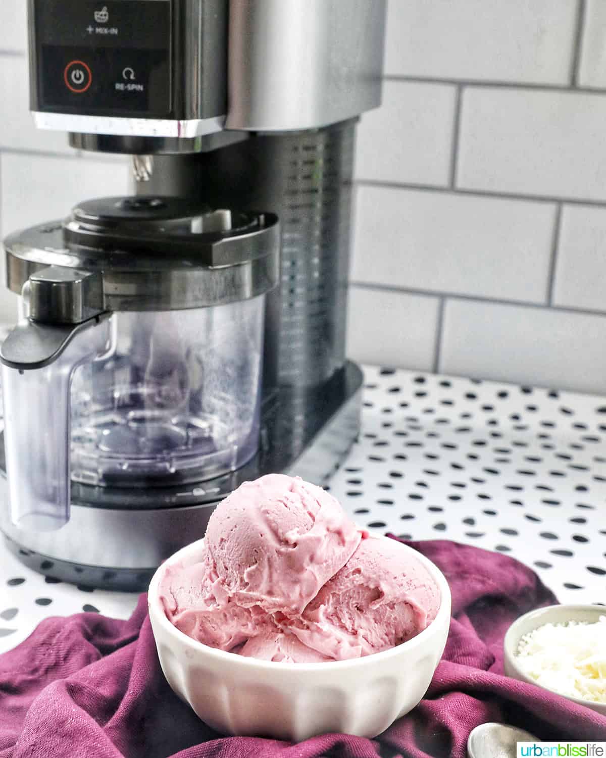 white bowl with scoops of purple ube ice cream topped with Ninja Creami ice cream machine in the background.