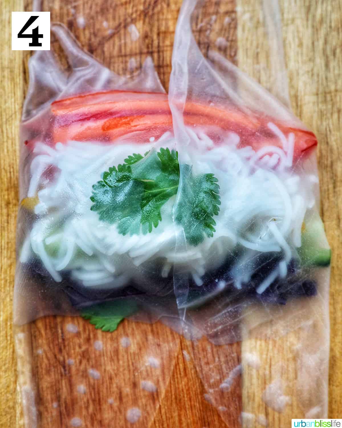 rice paper roll topped with vermicelli rice noodles and sliced colorful vegetables on a wooden cutting board.