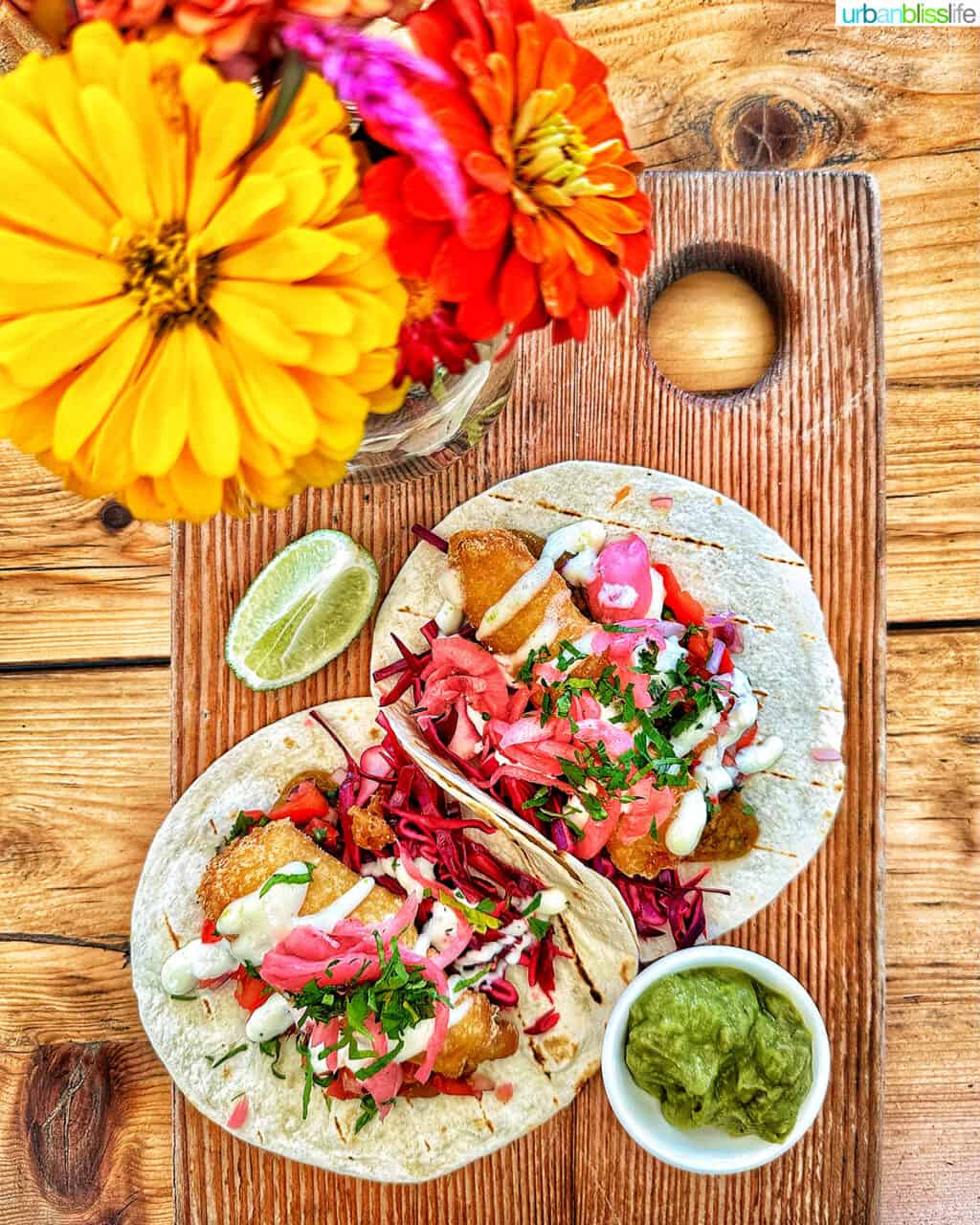 two fish tacos on a wooden board with colorful flowers at 10Acres Bistro in Victoria BC Canada.