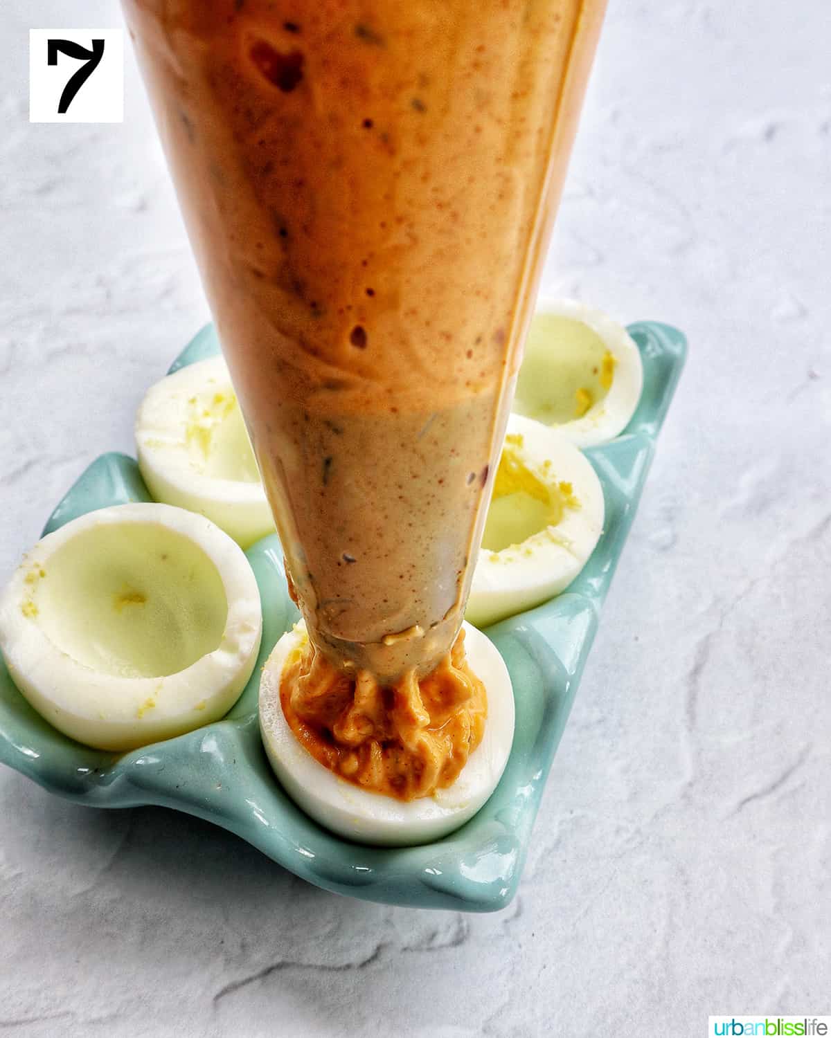 crab deviled egg filling in piping bag being piped into empty had boiled egg whites.