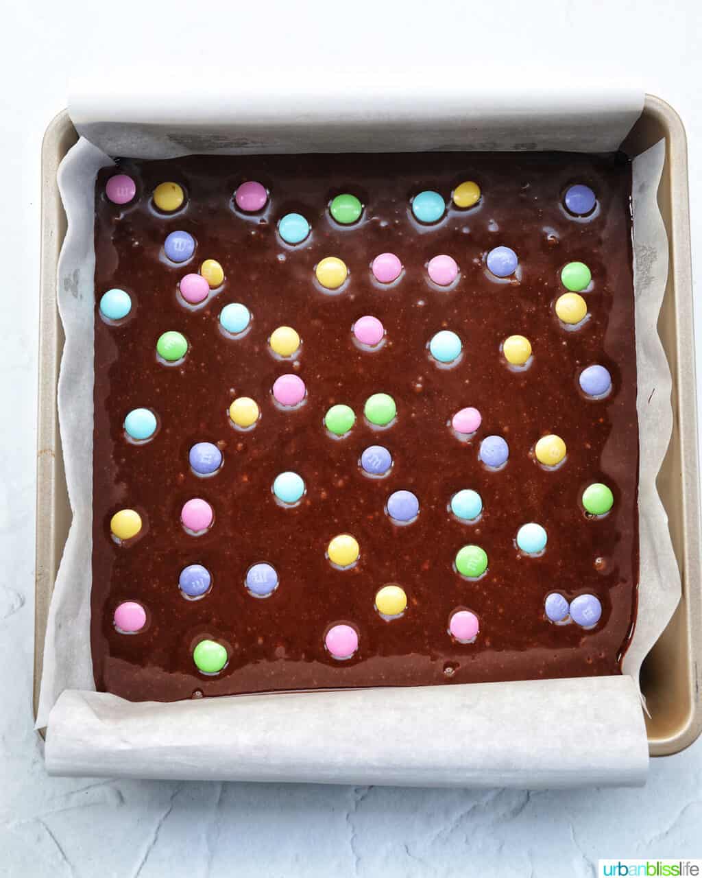 brownie batter in a square baking pan with pastel Easter M & Ms dotted on top.