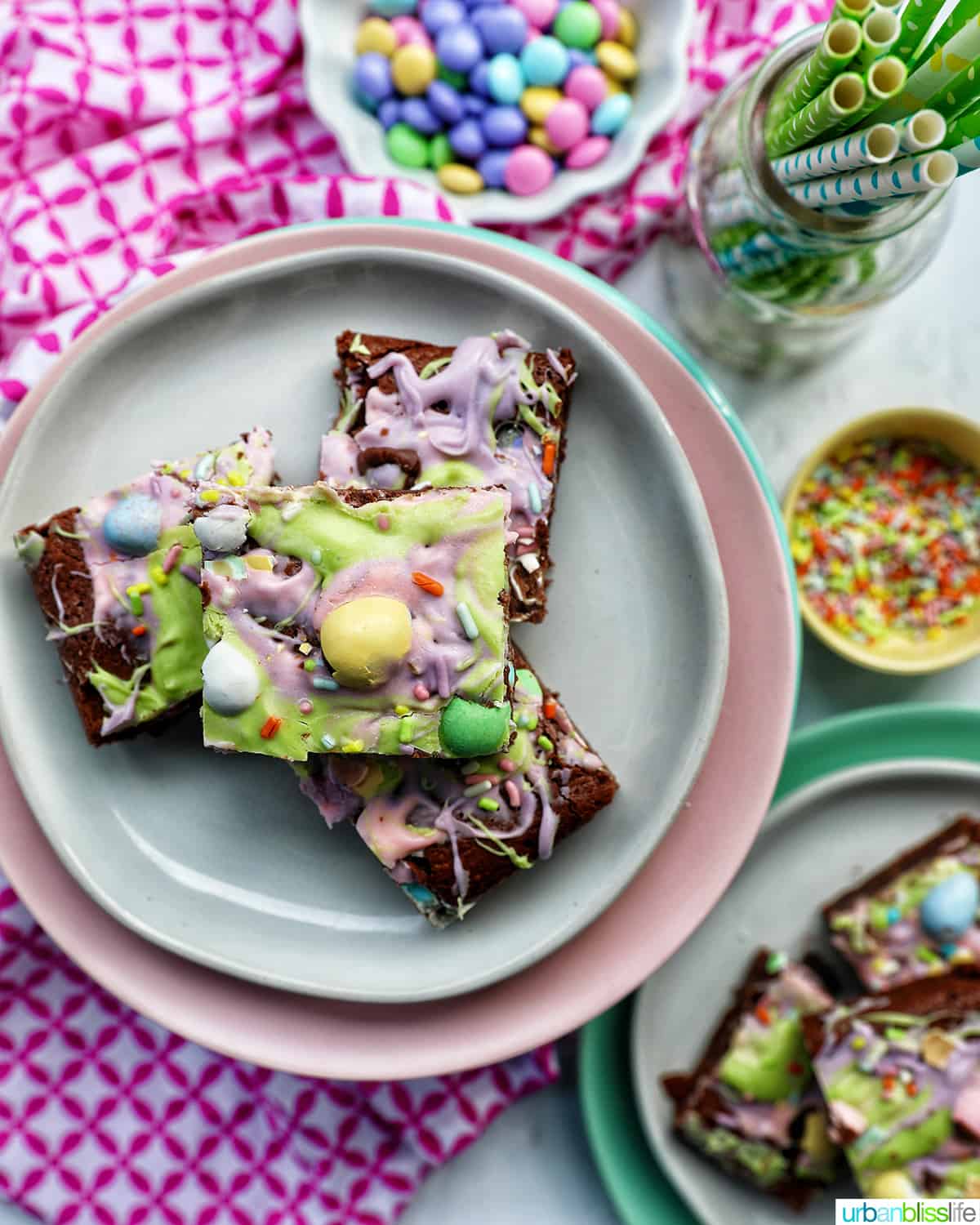 stacks of colorful Easter brownies on white and pink lates with sides of pastel M & Ms and sprinkles.