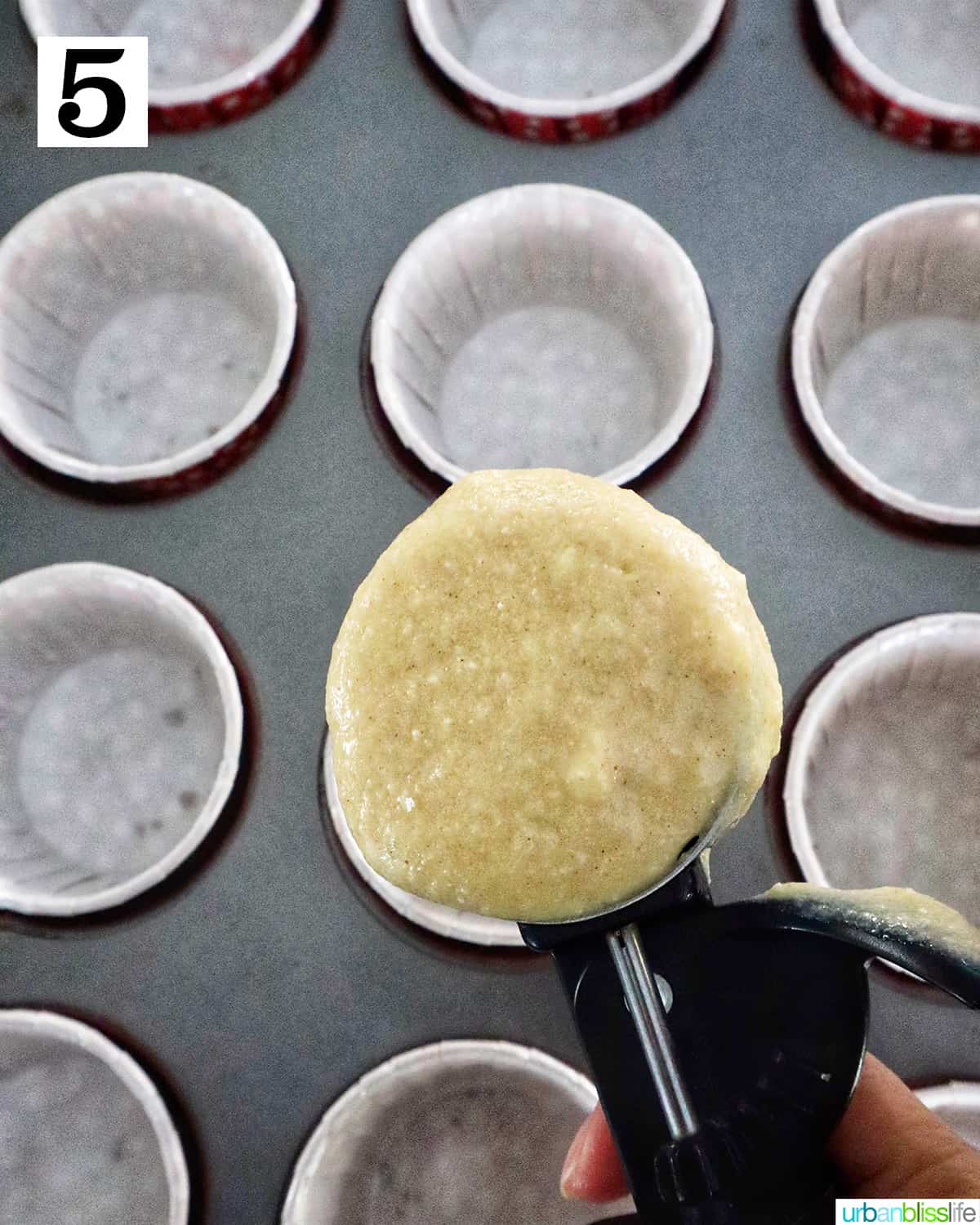 Cookie scoop with cupcake batter above a muffin tin with cupcake liners.