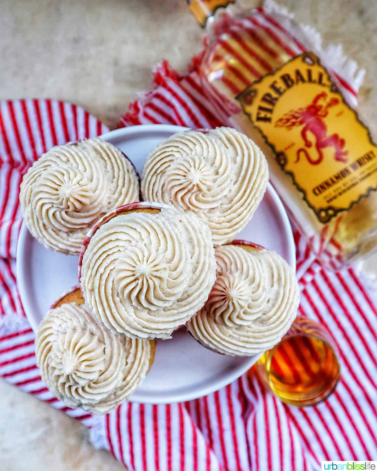 overhead photo of five cupcakes on a cake stand next to bottle of Fireball whiskey on a red and white napkin.