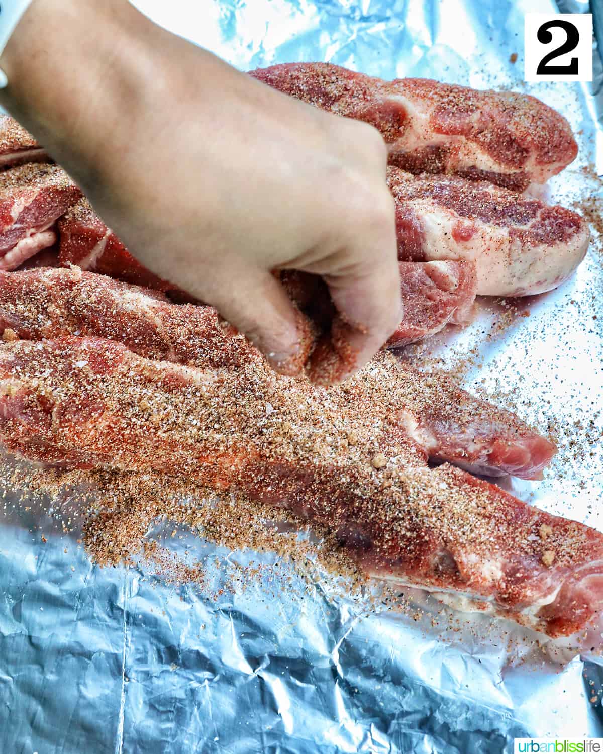 hand seasoning ribs on aluminum foil.