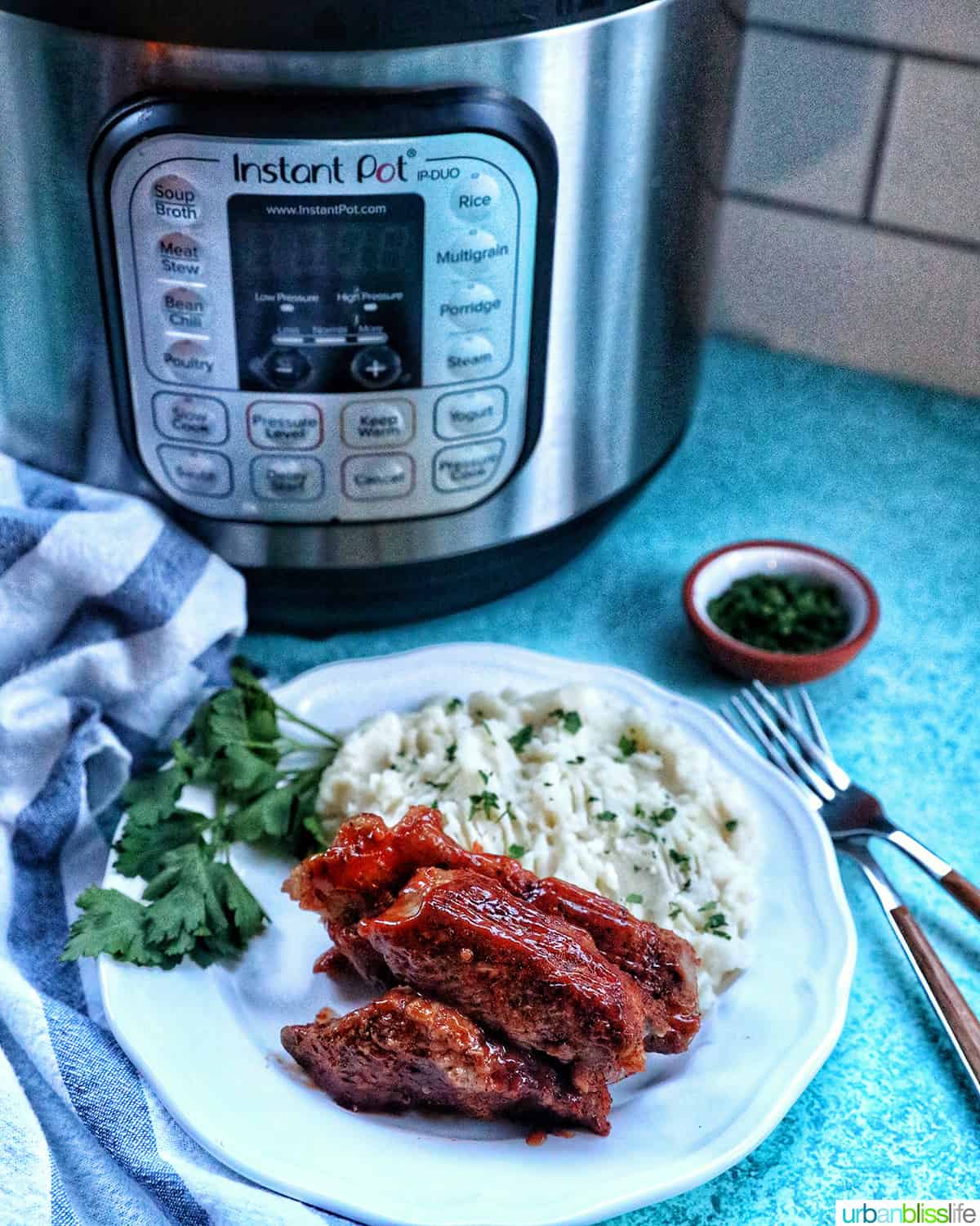 plate of Instant Pot country style ribs and mashed potatoes with herbs in front of an Instant Pot.