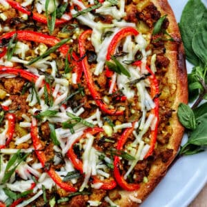 closeup of thai curry pizza toppings with sliced red peppers and sliced fresh basil.