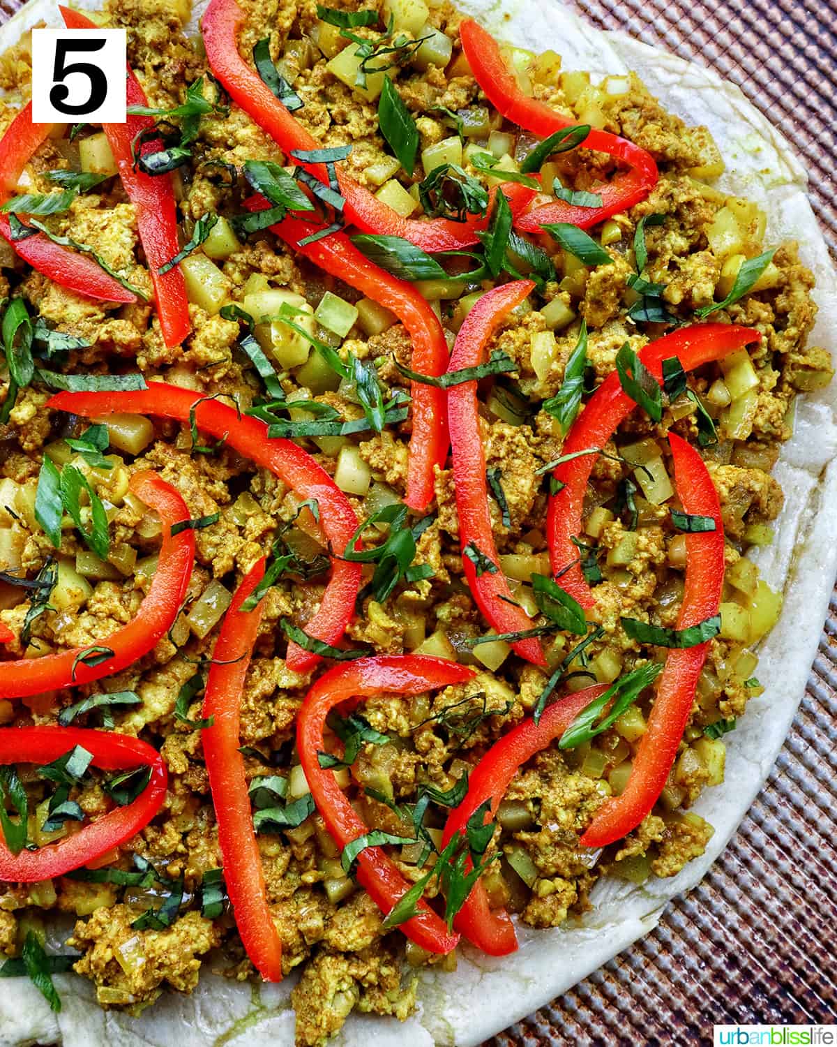 closeup of thai curry pizza toppings with sliced red peppers and sliced fresh basil.