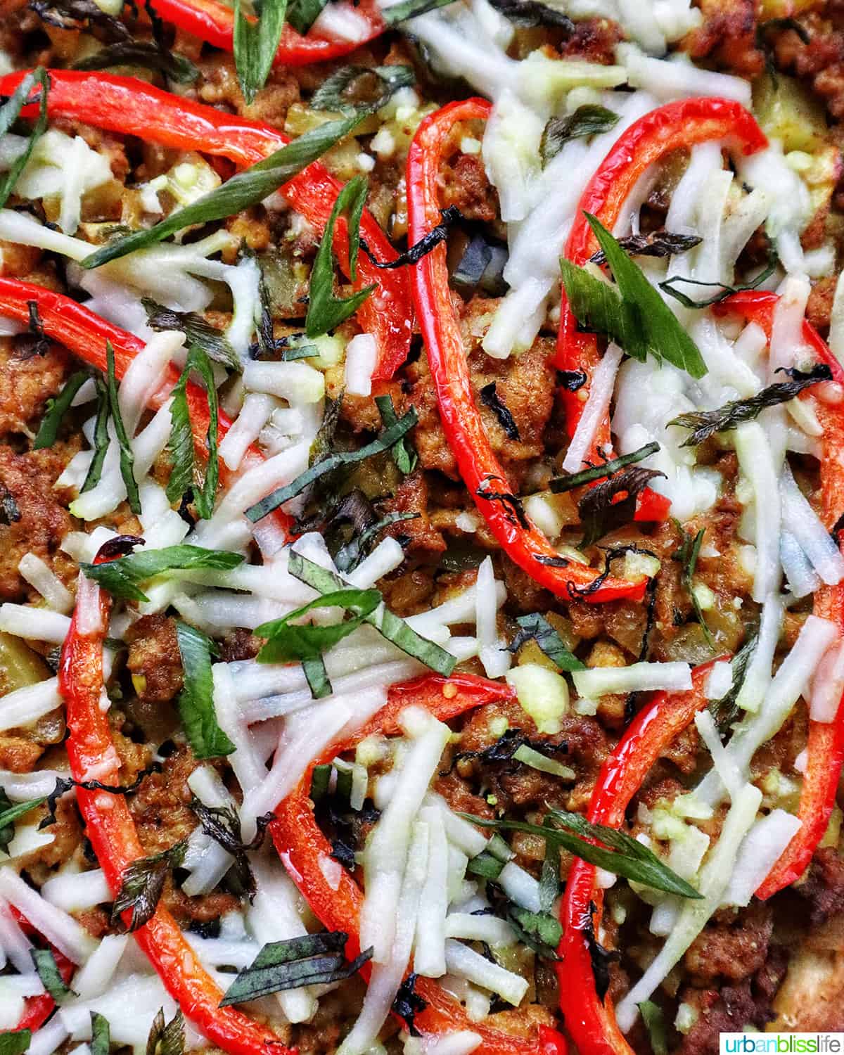 closeup of thai curry pizza toppings with sliced red peppers and sliced fresh basil and dairyfree mozzarella..