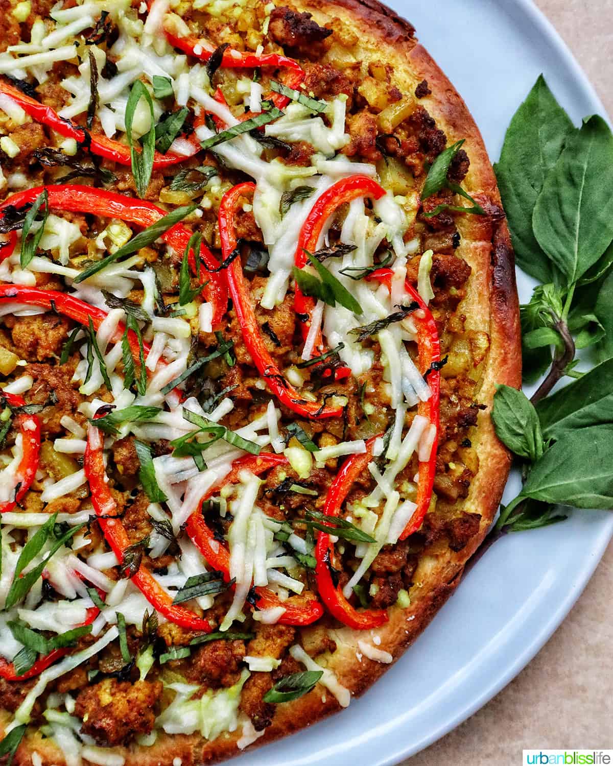 Thai curry pizza on a white plate with side of Thai basil.