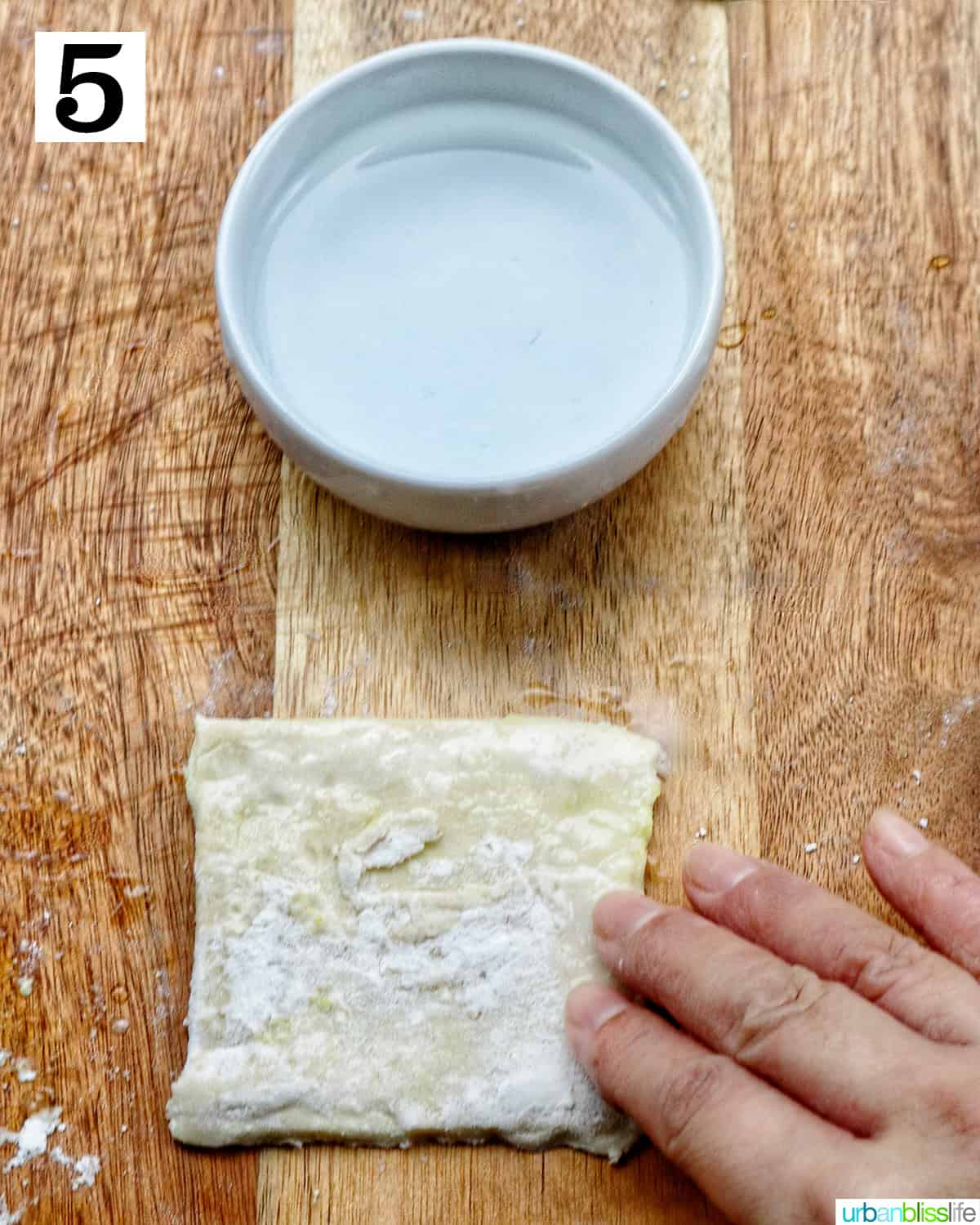 hand placing water around edges of a puff pastry square on cutting board.