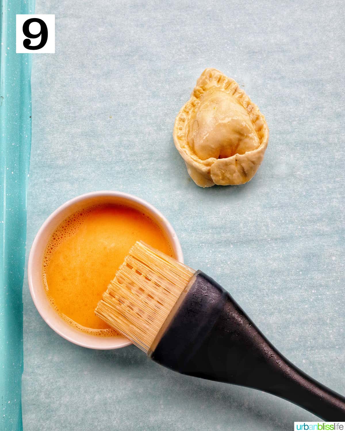 pastry brush, bowl of egg wash, and single Thai curry puff.