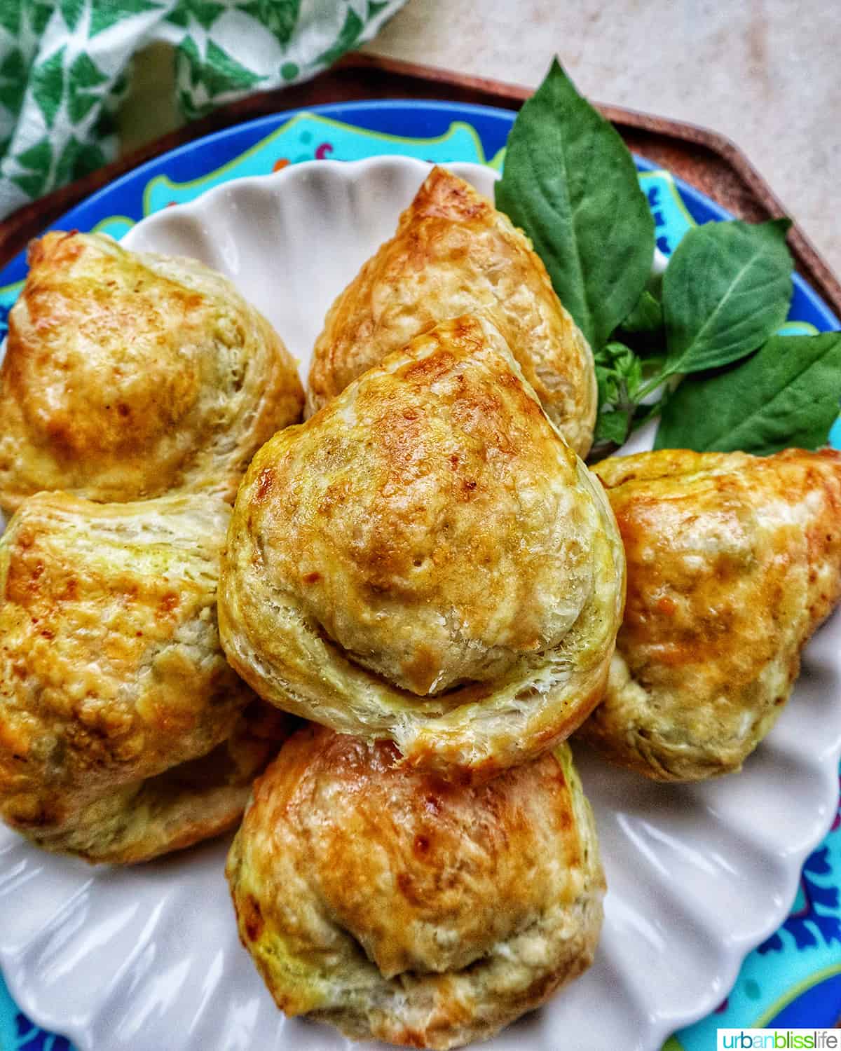 several baked Thai curry puff appetizers on a plate with side of Thai basil.