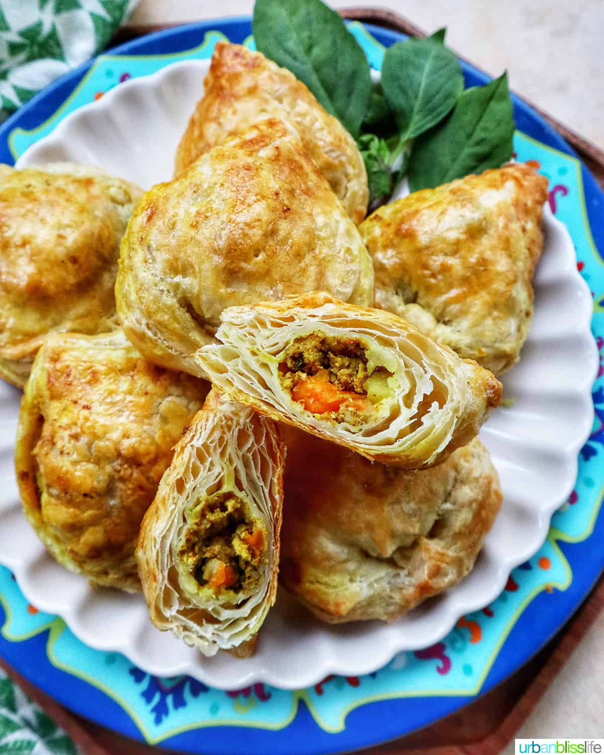 several baked Thai curry puff appetizers on a plate with side of Thai basil.