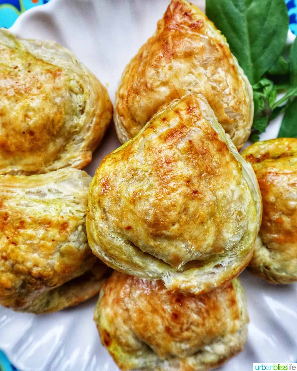 several baked Thai curry puff appetizers on a plate with side of Thai basil.