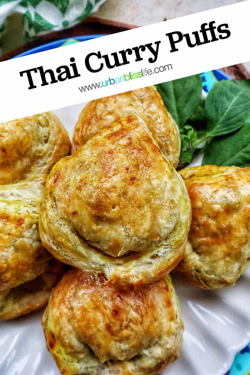 several baked Thai curry puff appetizers on a plate with side of Thai basil with text that reads Thai Curry Puffs.