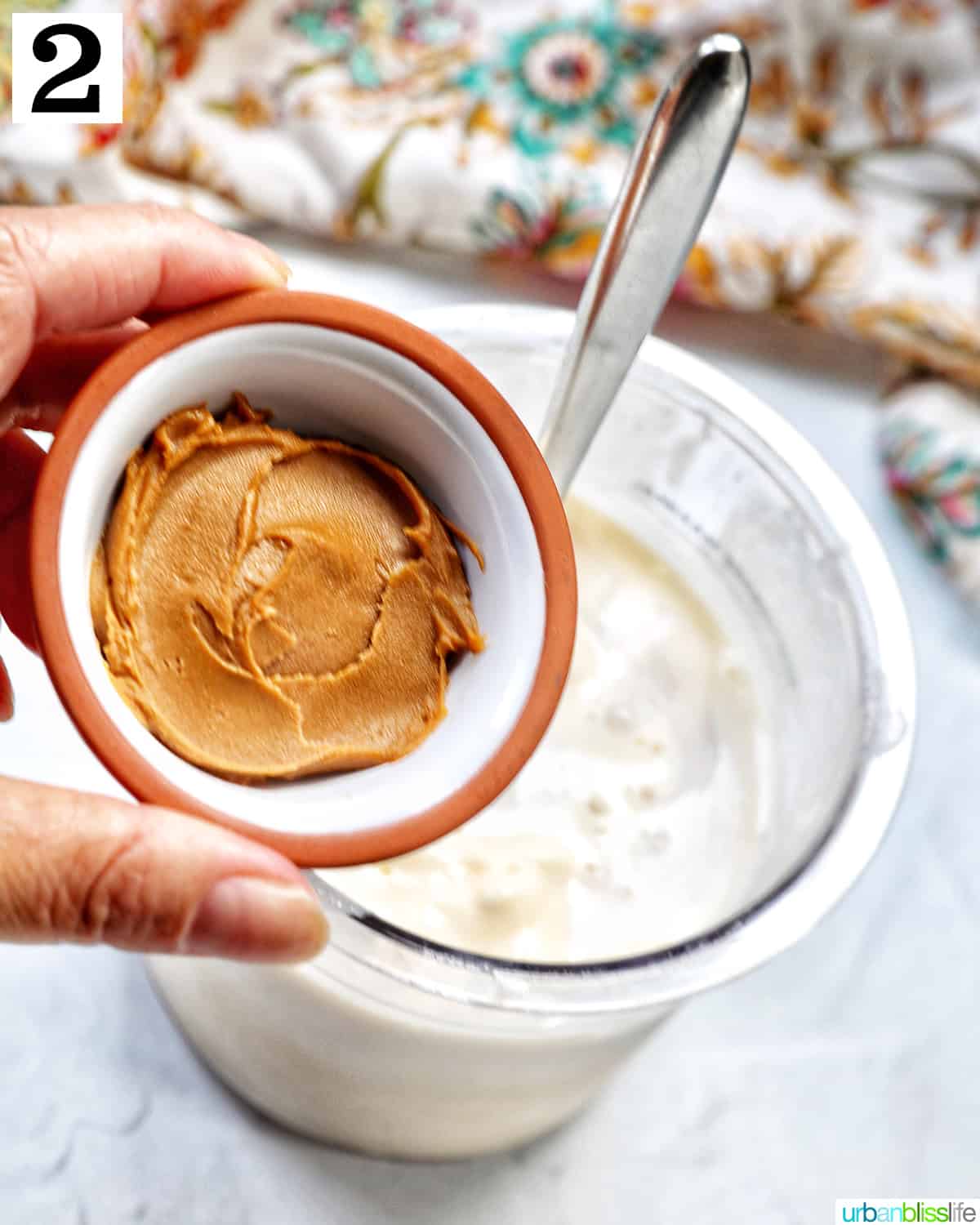 Hand holding a small bowl of Biscoff spread over a pint container of vanilla ice cream.