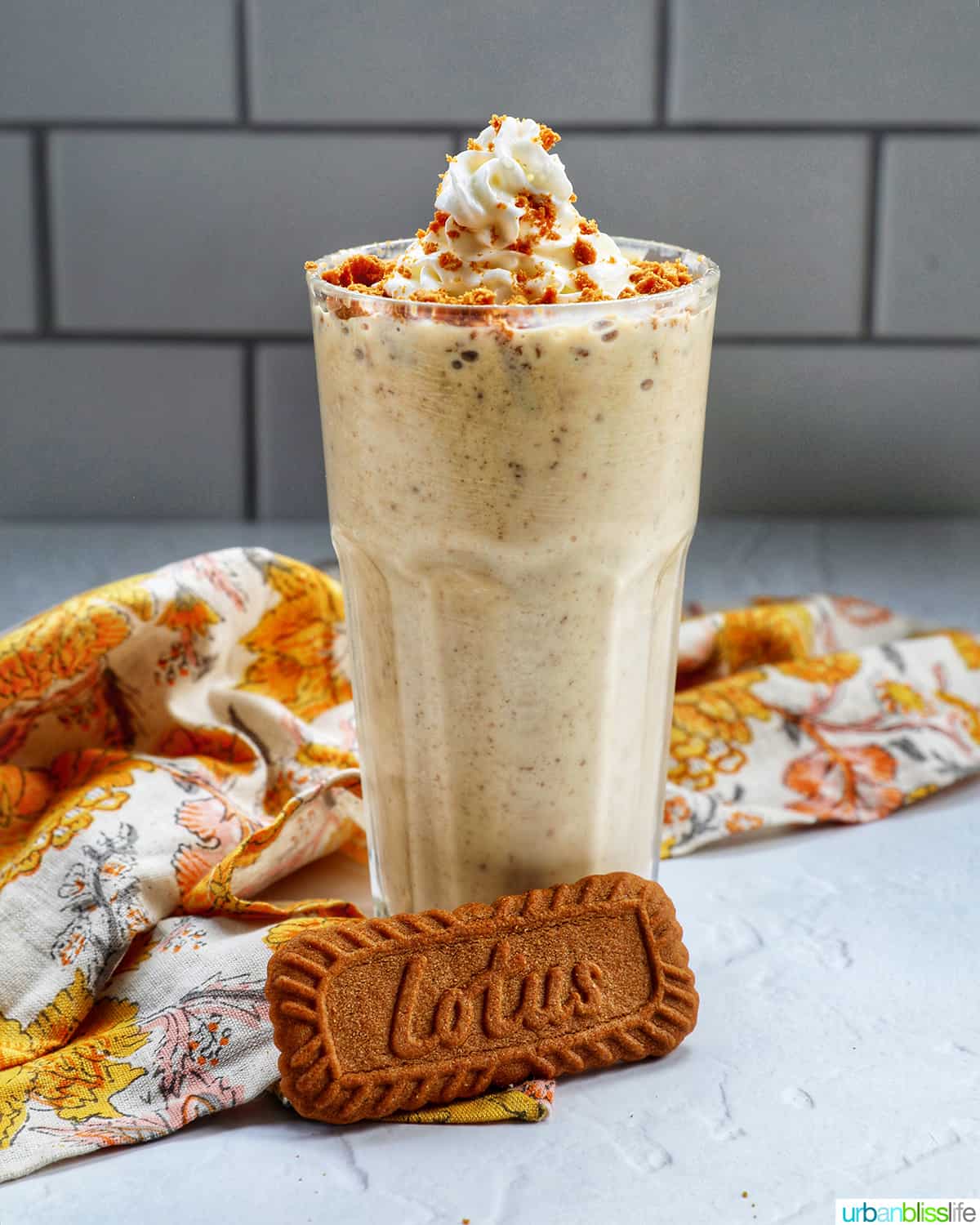 Biscoff Milkshake in a milkshake glass with a yellow floral kitchen linen and biscoff cookie.