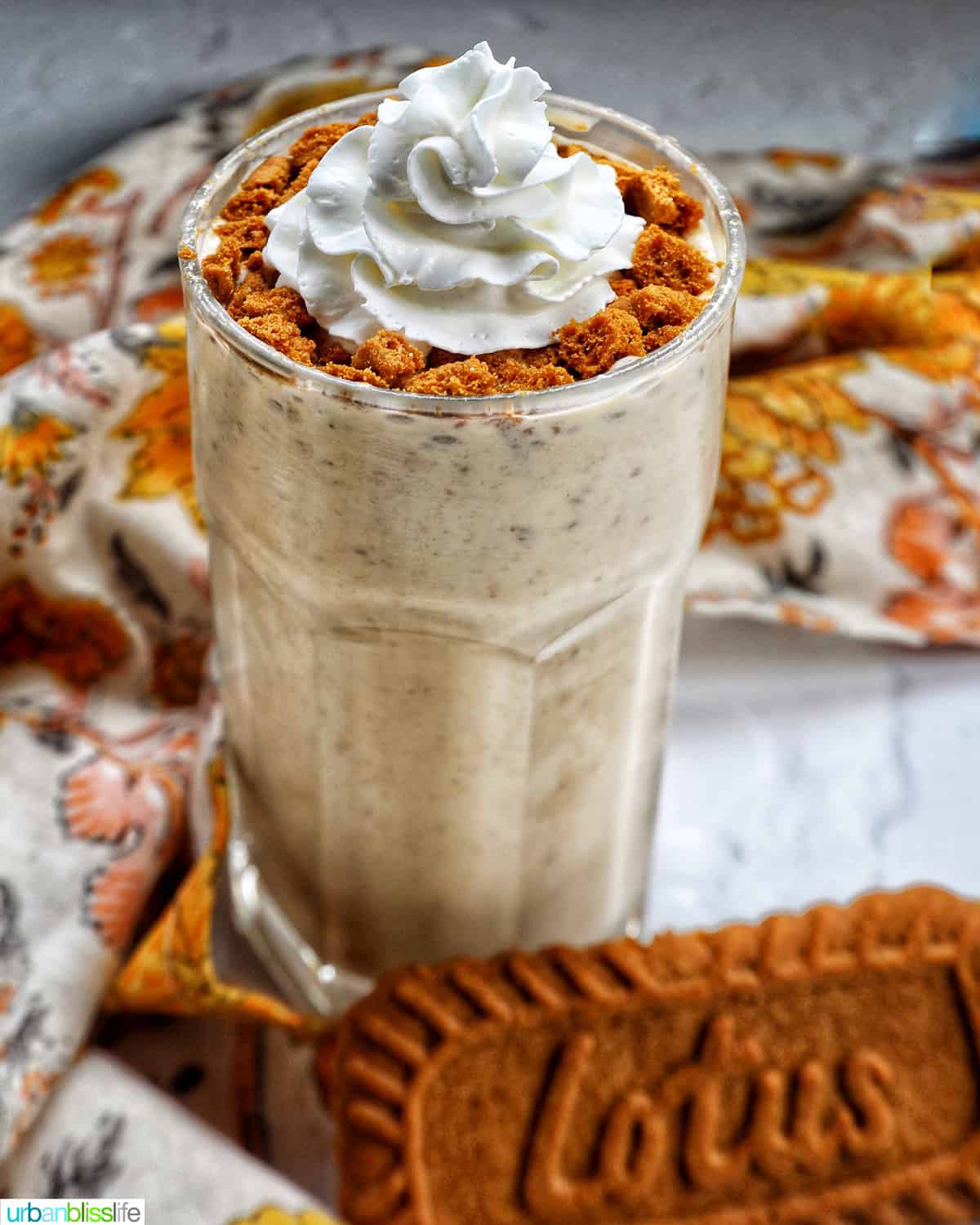 Biscoff Milkshake in a milkshake glass with a yellow floral kitchen linen and biscoff cookie.