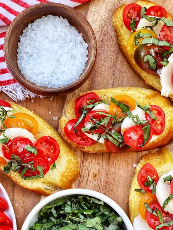 crostini with tomatoes, mozzarella, basil surrounded by plates of the same toppings and a bowl of sea salt.