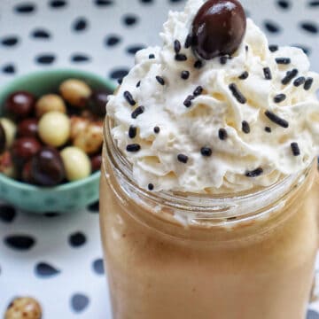 coffee milkshake in a mason jar mug with whipped cream and chocolate covered espresso beans on a polka dot table.
