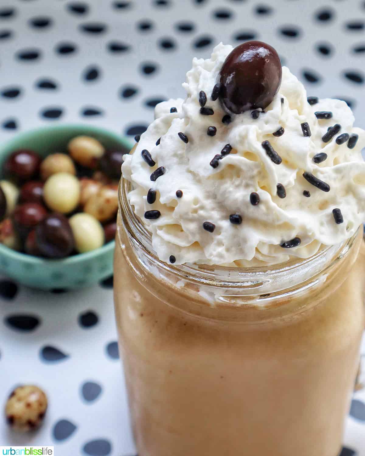 coffee milkshake in a mason jar mug with whipped cream and chocolate covered espresso beans on a polka dot table.