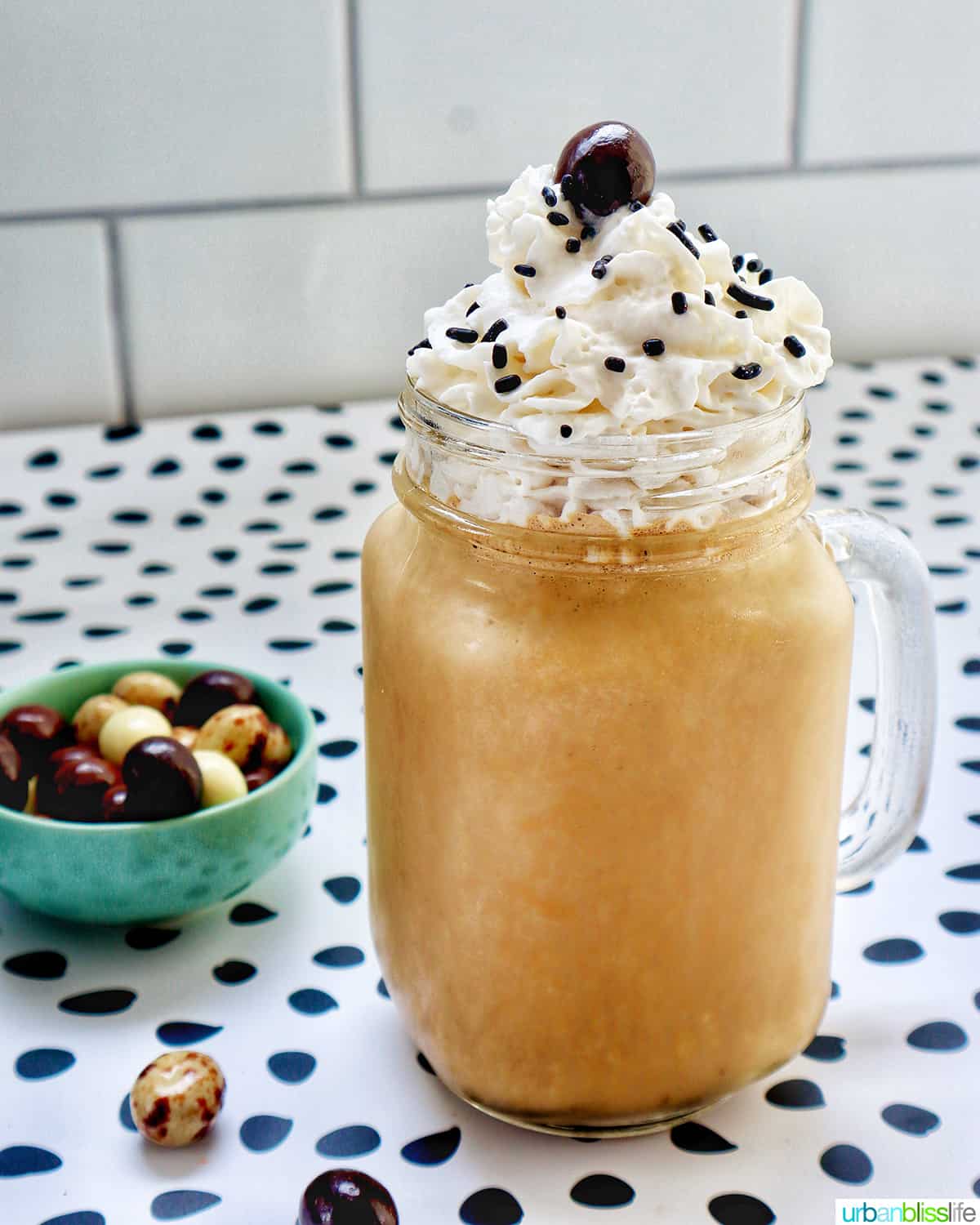 coffee milkshake in a mason jar mug with whipped cream and chocolate covered espresso beans on a polka dot table.