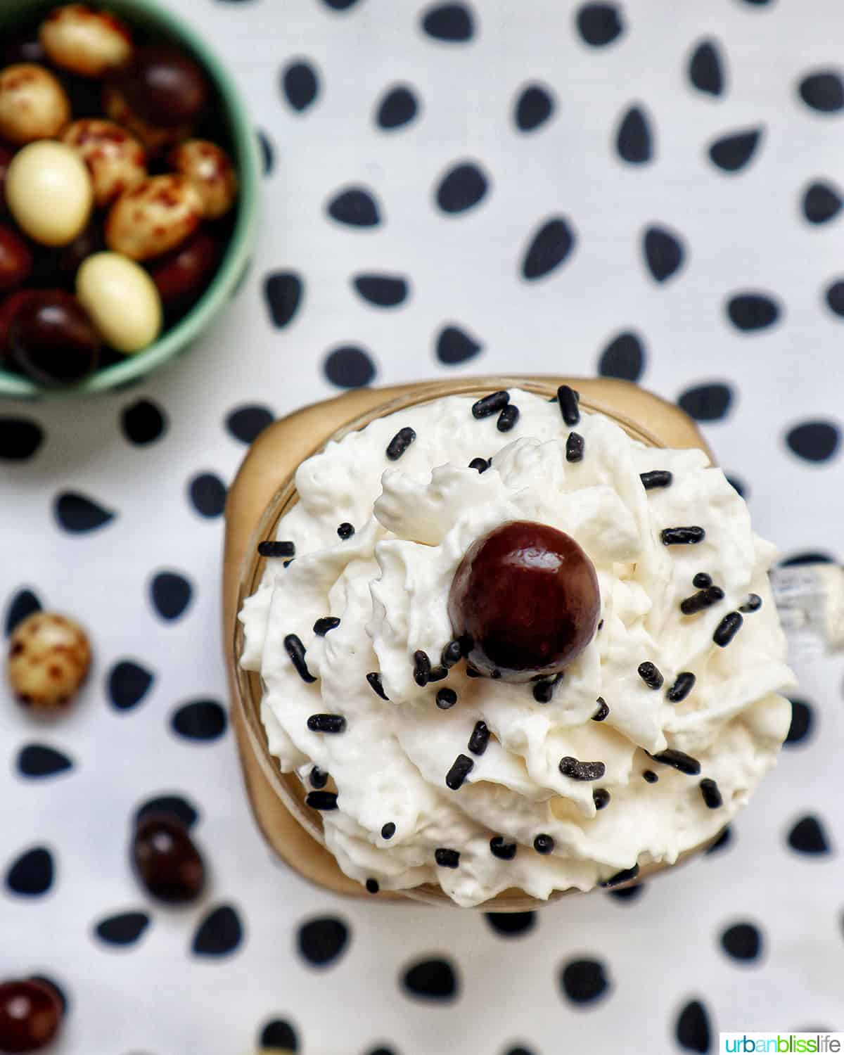 coffee milkshake in a mason jar mug with whipped cream and chocolate covered espresso beans on a polka dot table.