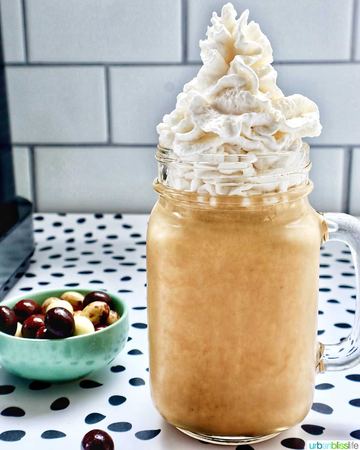 coffee milkshake in a mason jar mug with whipped cream and chocolate covered espresso beans on a polka dot table.