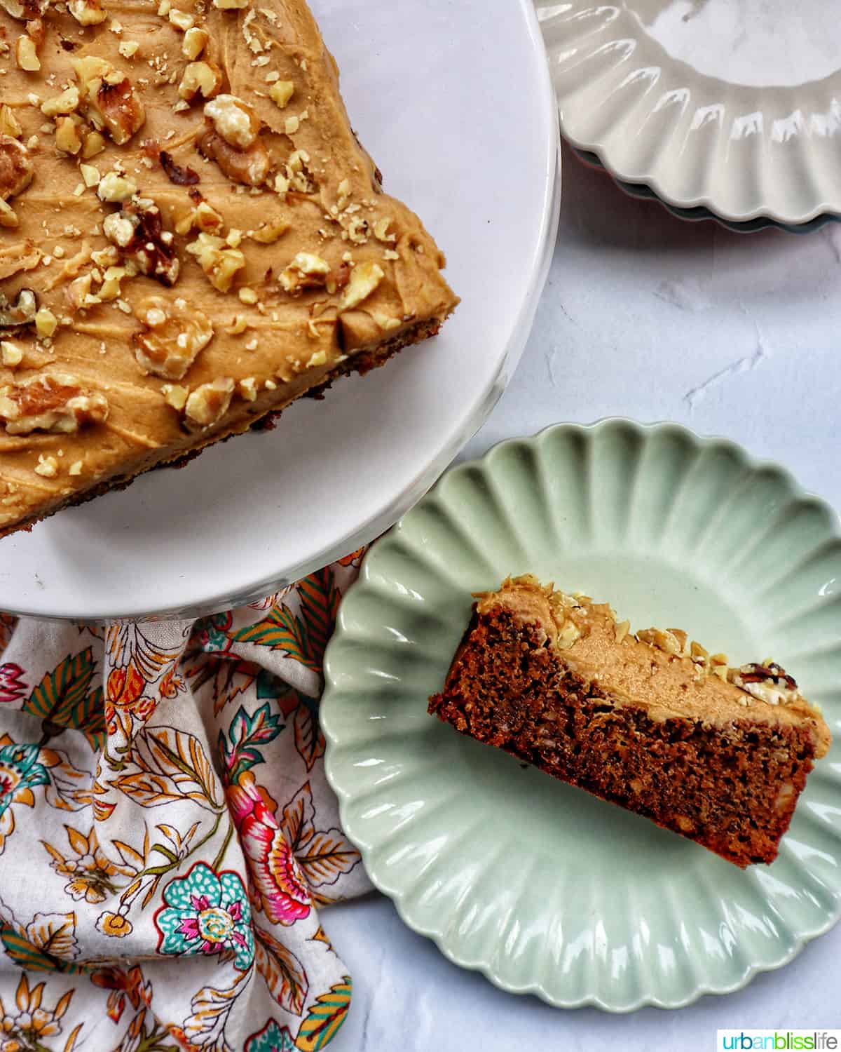 slice of coffee walnut loaf on a green plate next to a whole coffee walnut loaf on a cake pedestal.