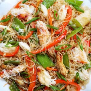 crab pancit filipino noodles in a large bowl, with slices veggies and chunks of crab meat.