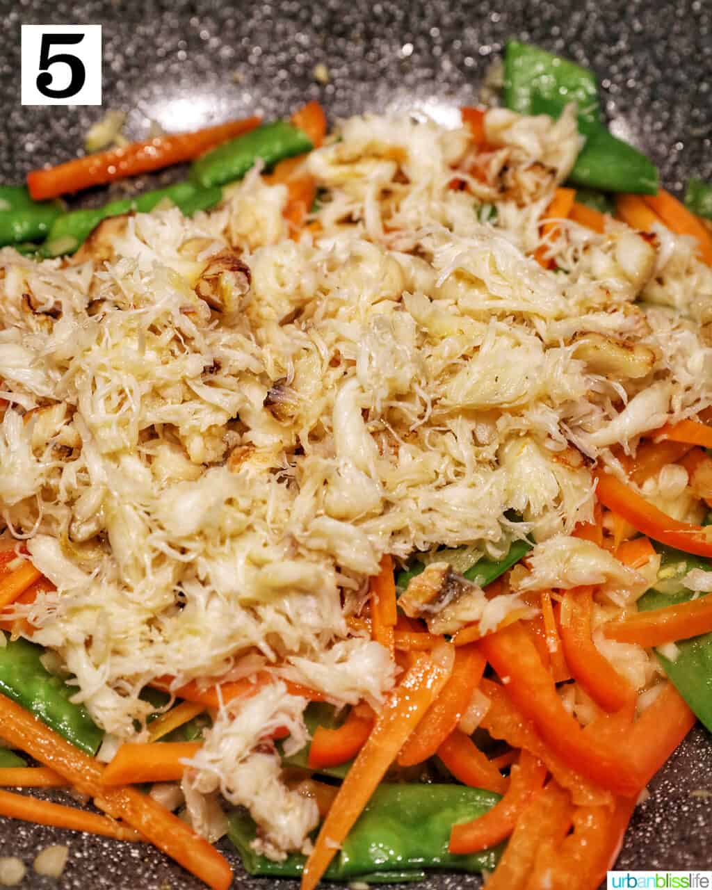 adding cooked crab meat back to the wok with vegetables.